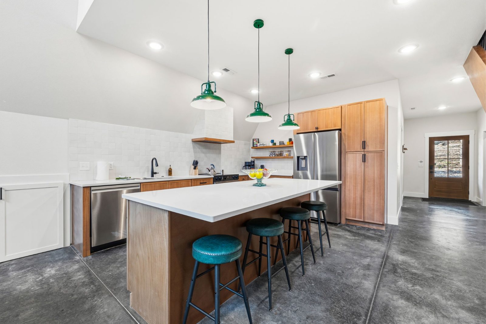 The full kitchen with island, bar stools, pendant lights, and the back door view