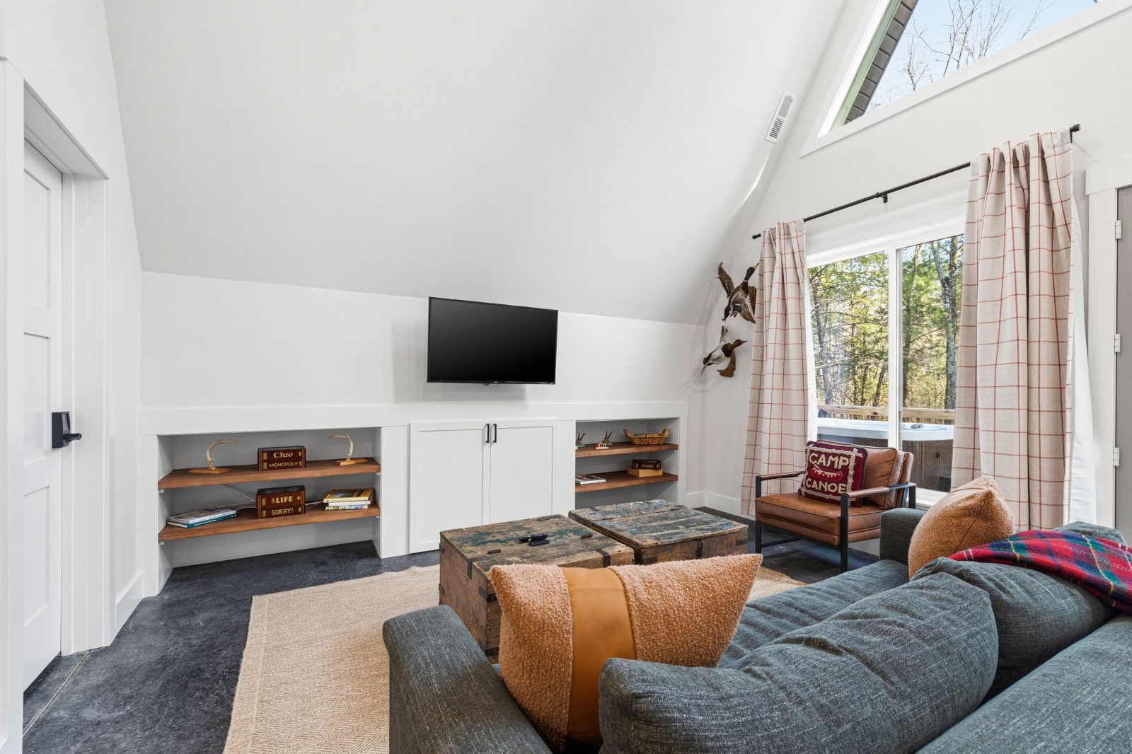 The living room with TV, leather chair, board games shelves, and trunk-style coffee tables
