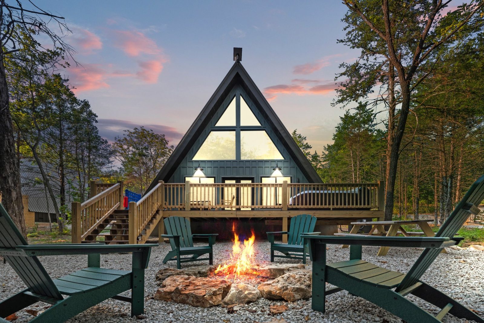 The A-frame cabin at sunset with the fire pit lit and Adirondack chairs